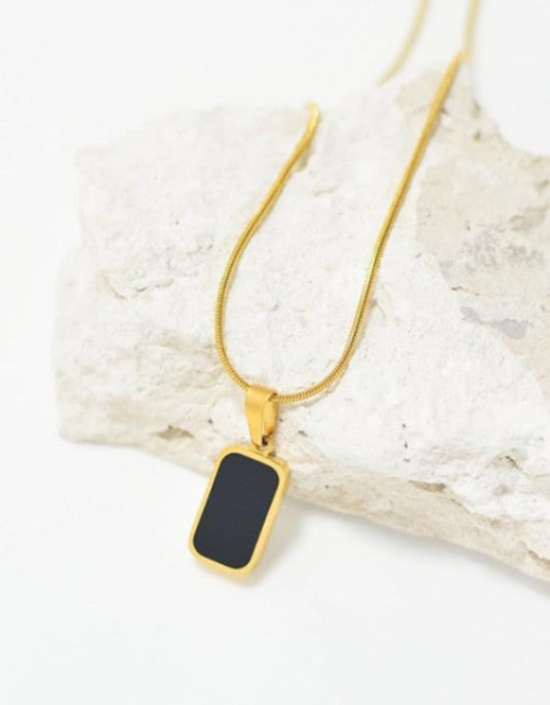 Gold necklace with a black pendant on a textured white surface