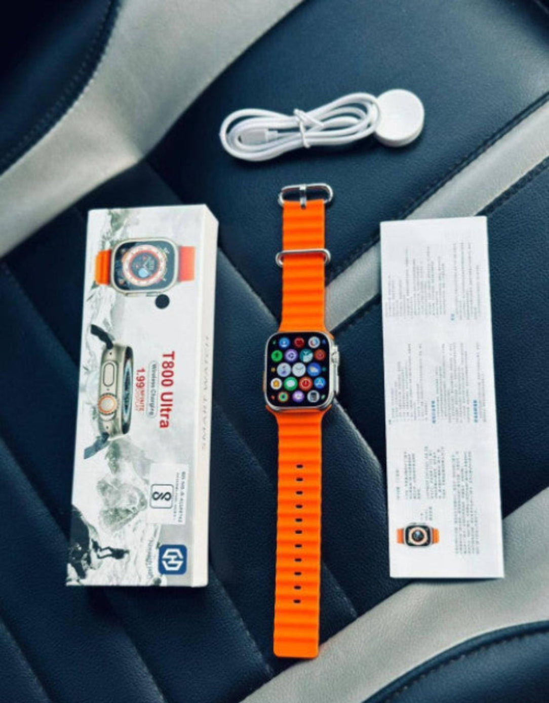 Smartwatch with orange band, box, cable, and paper on a car seat