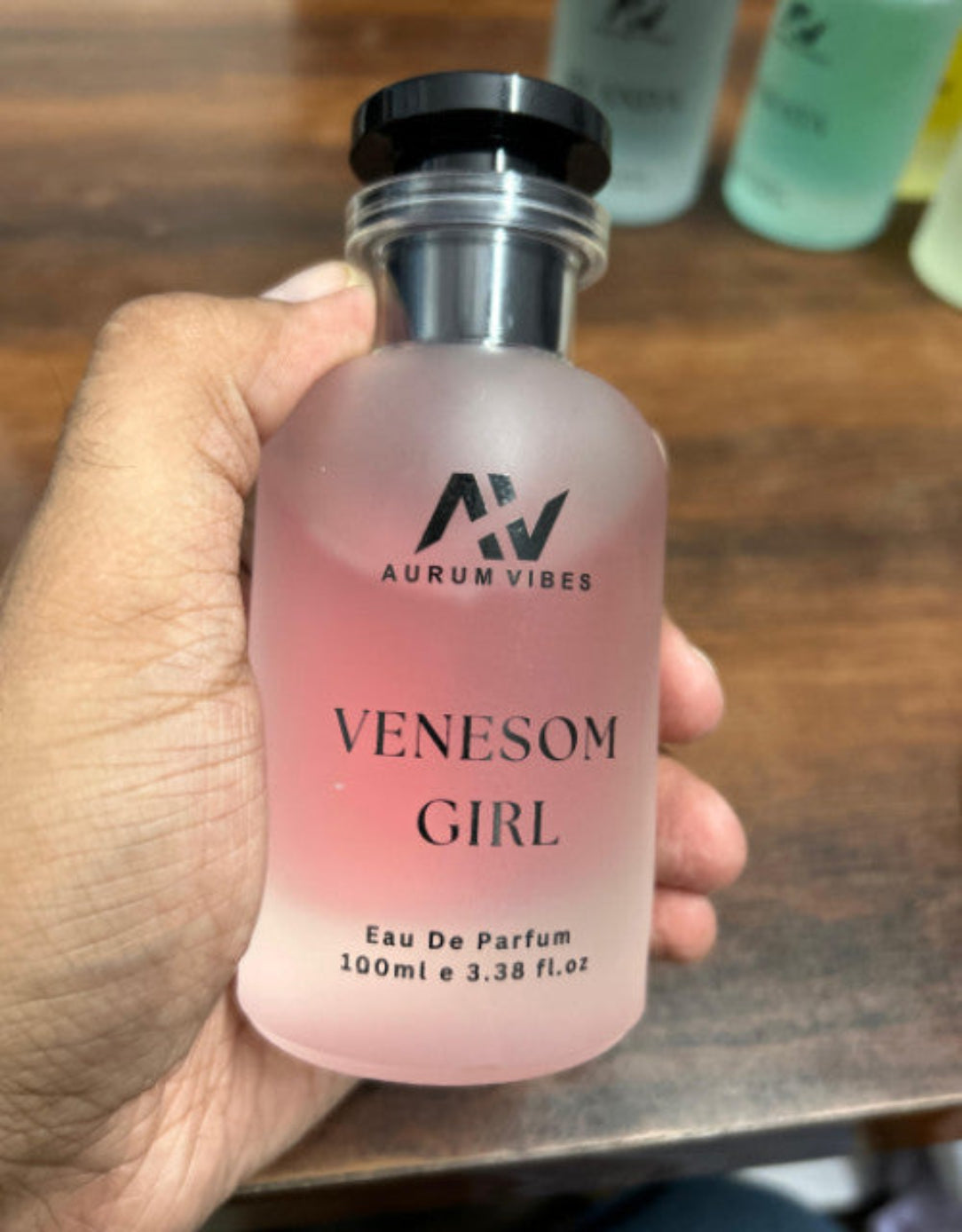 Hand holding a 'Venesom Girl' eau de parfum bottle with 'Aurum Vibes' branding.