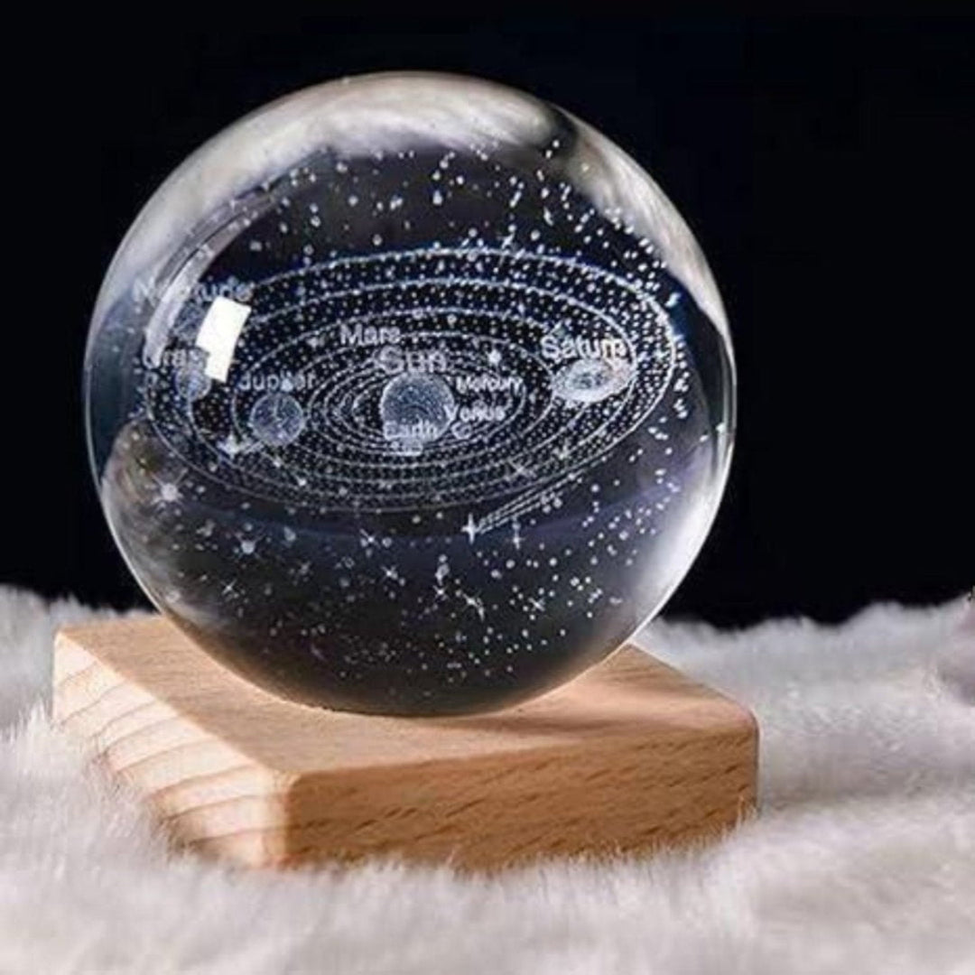 Glass sphere with solar system model on a wooden stand against a dark background