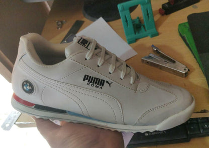 White Puma sneaker with BMW logo held by a hand on a cluttered surface.