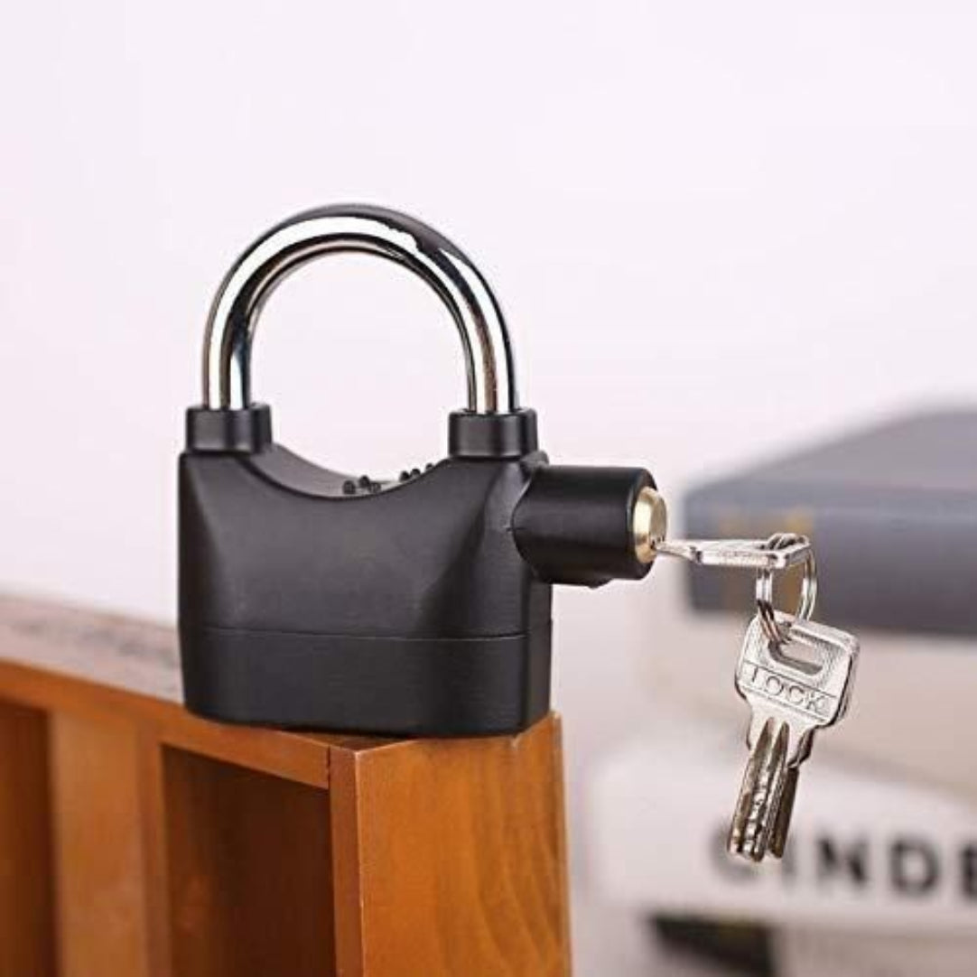 A black metal padlock with a built-in siren alarm, featuring a key inserted in the lock, displayed on a wooden surface.