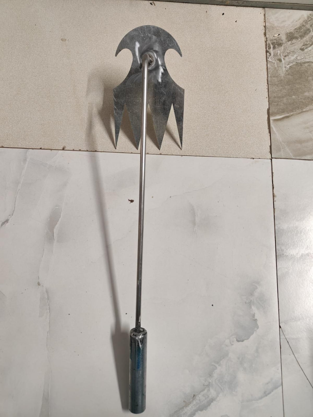 Metal tool with a curved blade and handle on a tiled floor
