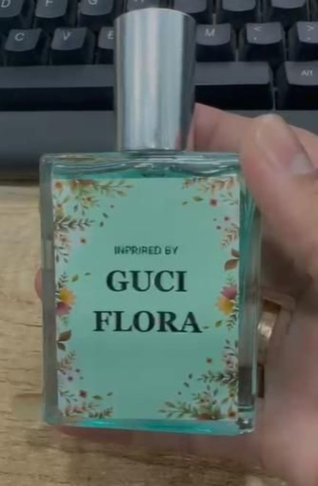 Perfume bottle labeled 'Gucci Flora' held by a hand with a keyboard in the background.