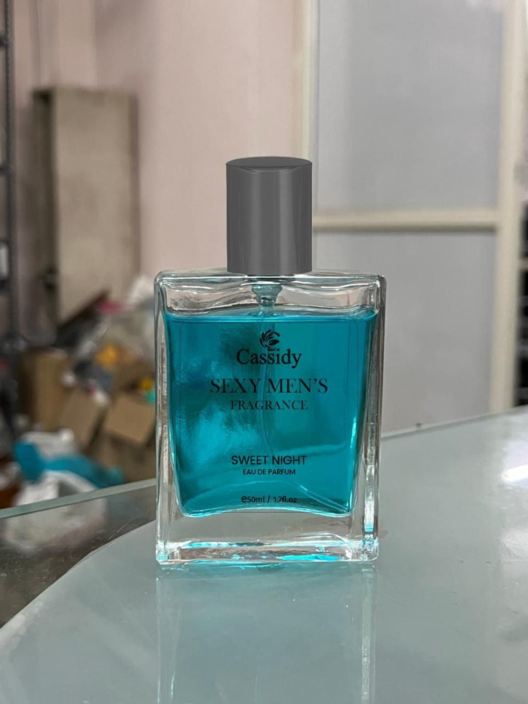 Blue perfume bottle labeled 'Cassidy Sexy Men's Fragrance Sweet Night' on a reflective surface.
