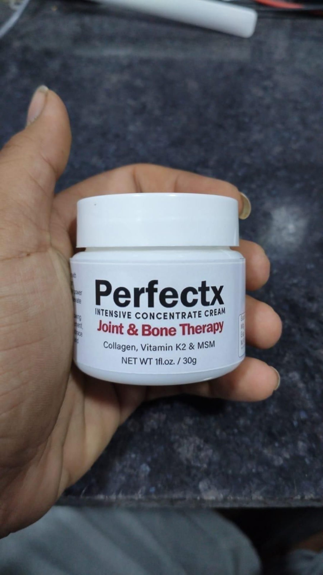 Hand holding a jar of Perfectx Intensive Concentrate Cream on a dark background