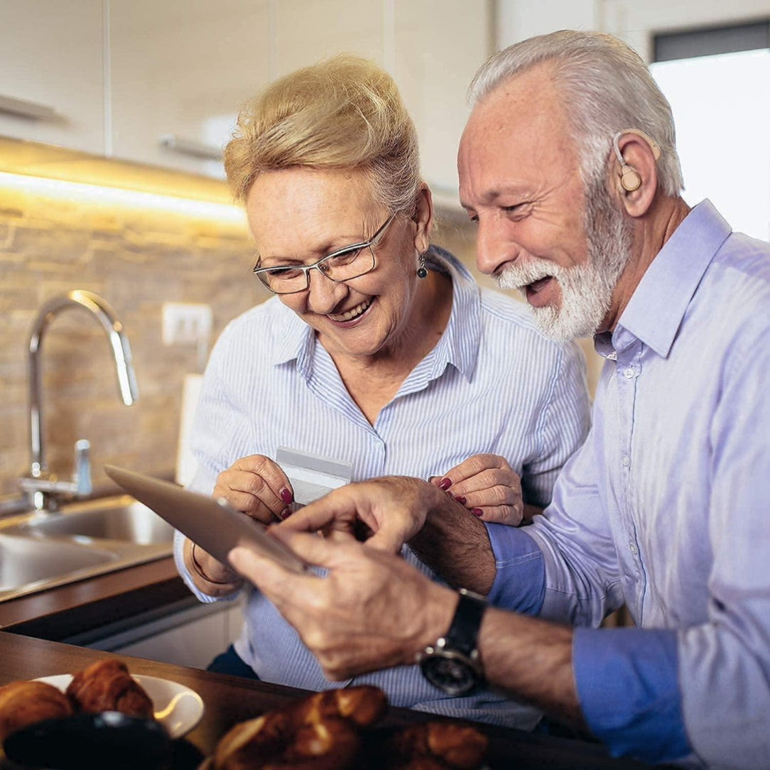 Two elderly people looking at a tablet together in a kitchen.