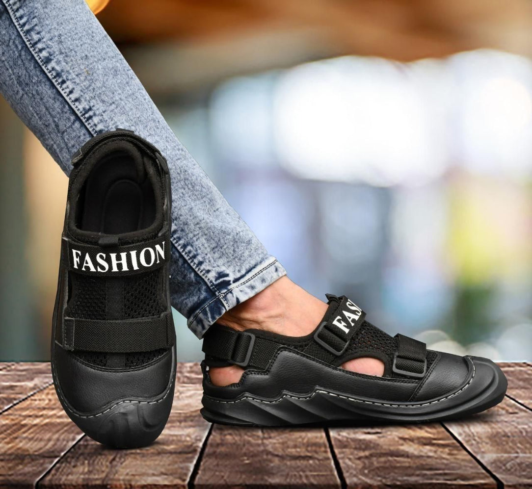 A person wearing casual jeans is showcasing a black sandal with the text 'FASHION' on it, indicating a casual dailywear sandal.