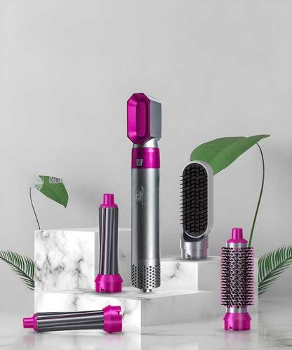 Set of hair styling tools with pink and silver accents on a marble surface with green leaves.