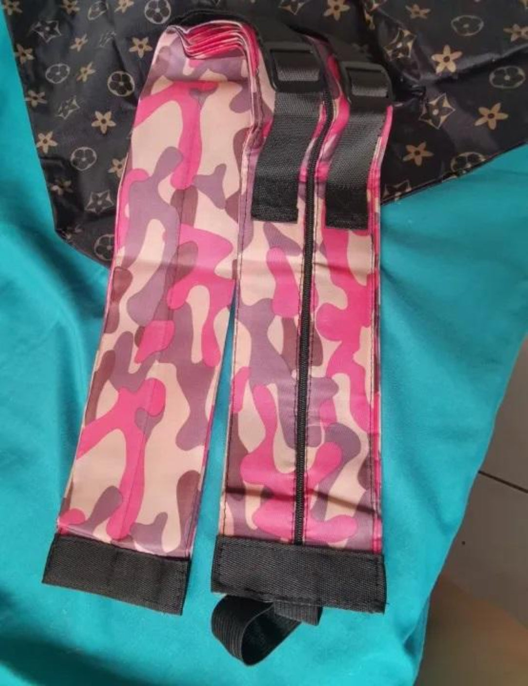 Pink camouflage straps with black edges on a teal surface