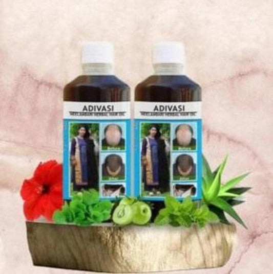 Two bottles of Adivasi Neelambari Herbal Hair Oil placed on a wooden surface with decorative flowers and herbs around them.
