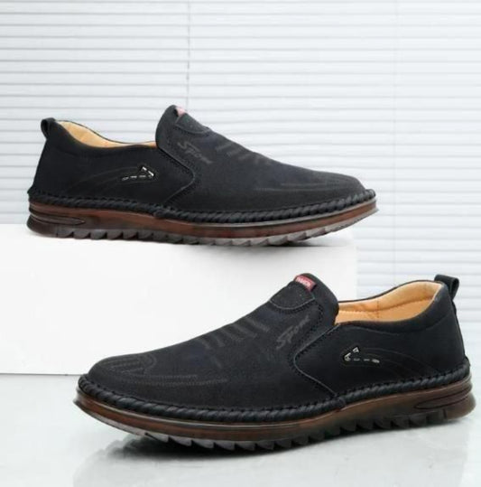 Pair of black slip-on shoes with brown soles on a white background