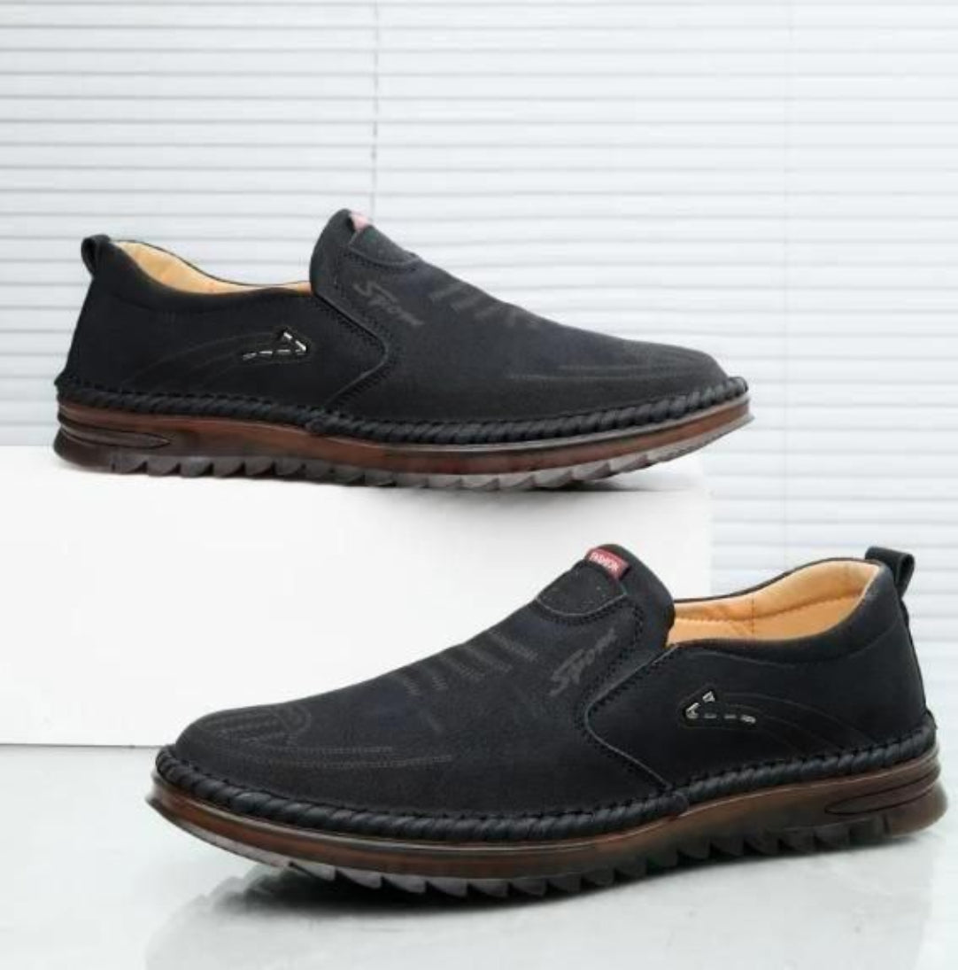 Pair of black slip-on shoes with brown soles on a white background