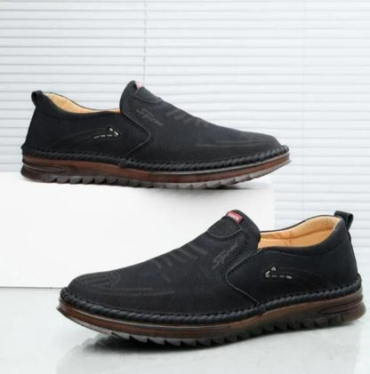 Pair of black slip-on shoes with brown soles on a white background