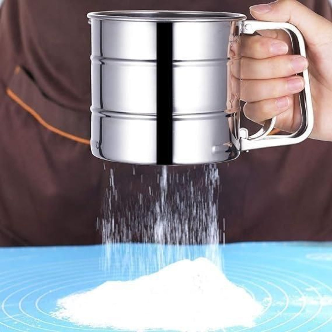 Metallic sifter being used to sift flour onto a blue surface.