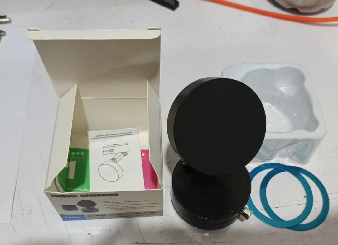 Black circular object next to an open box with product packaging on a white surface.
