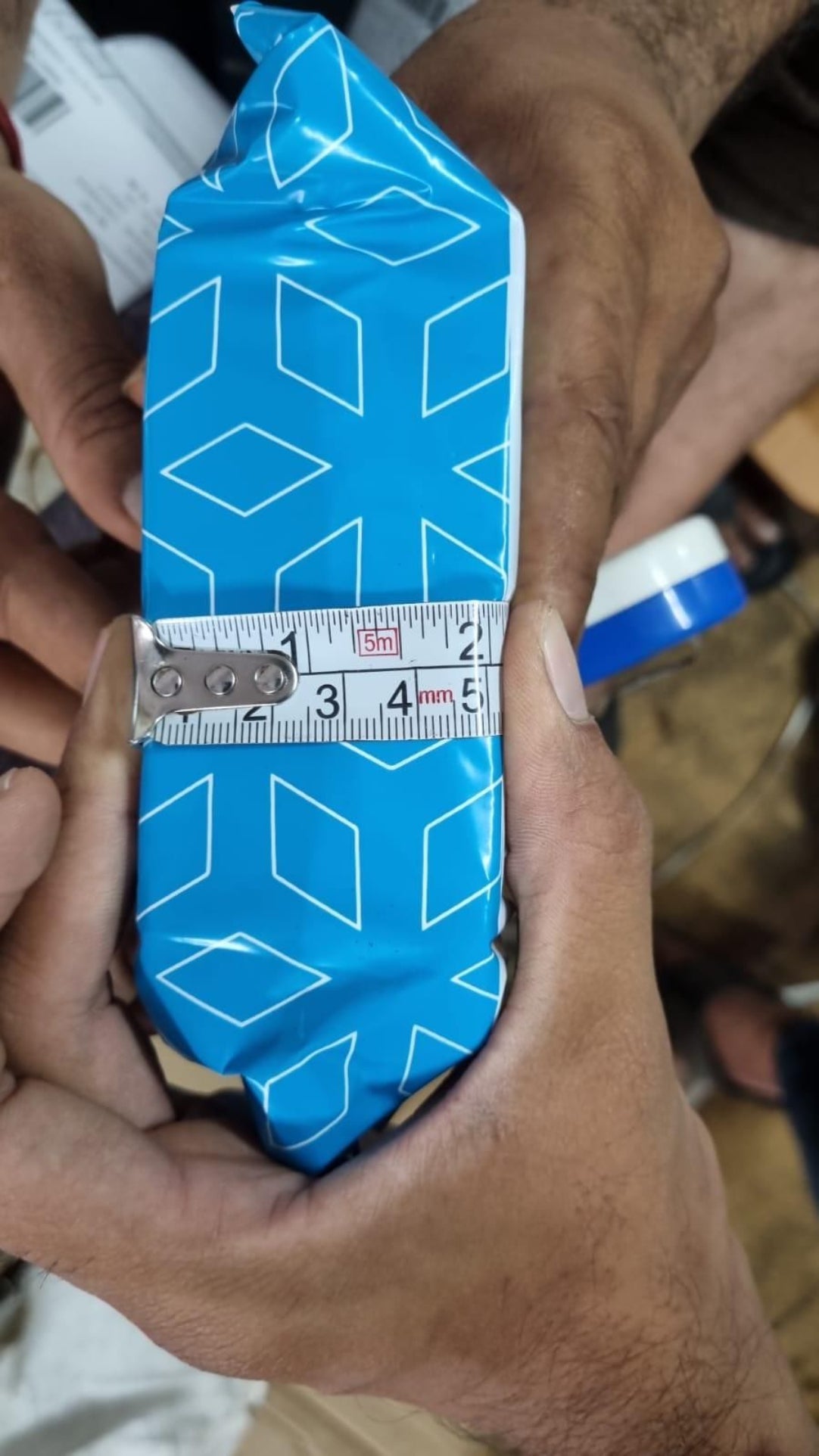 Blue geometric-patterned object being measured with a ruler
