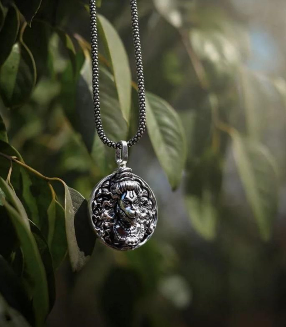 Silver pendant necklace with intricate design against a blurred green leafy background