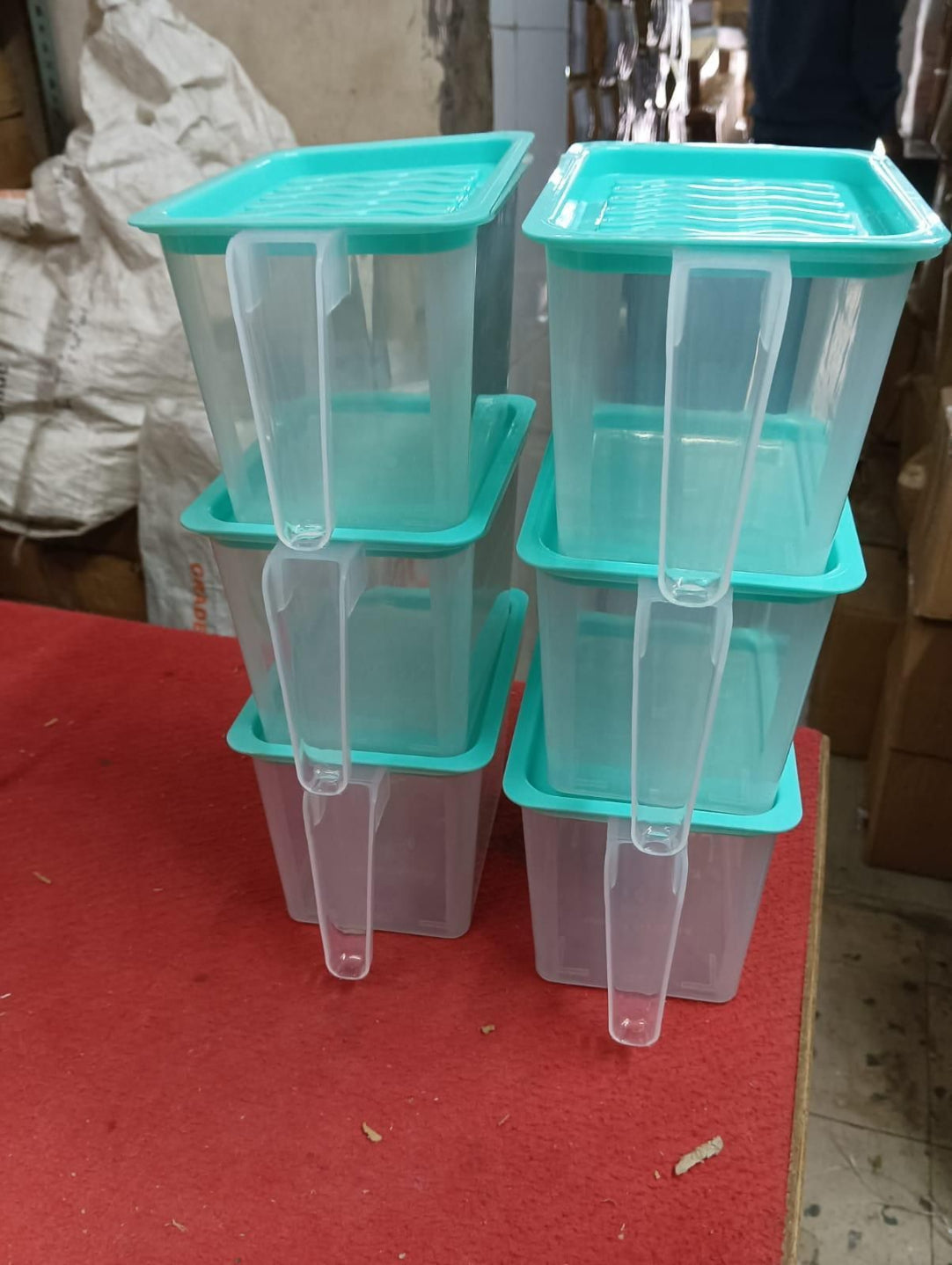Stack of clear plastic containers with green lids on a red surface.