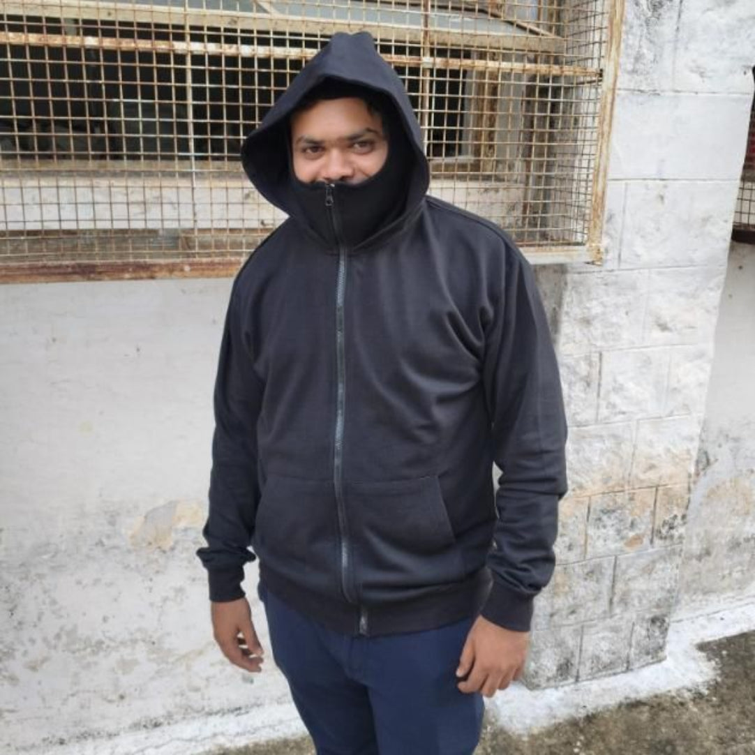 Person wearing a dark hoodie and blue pants standing against a textured wall.