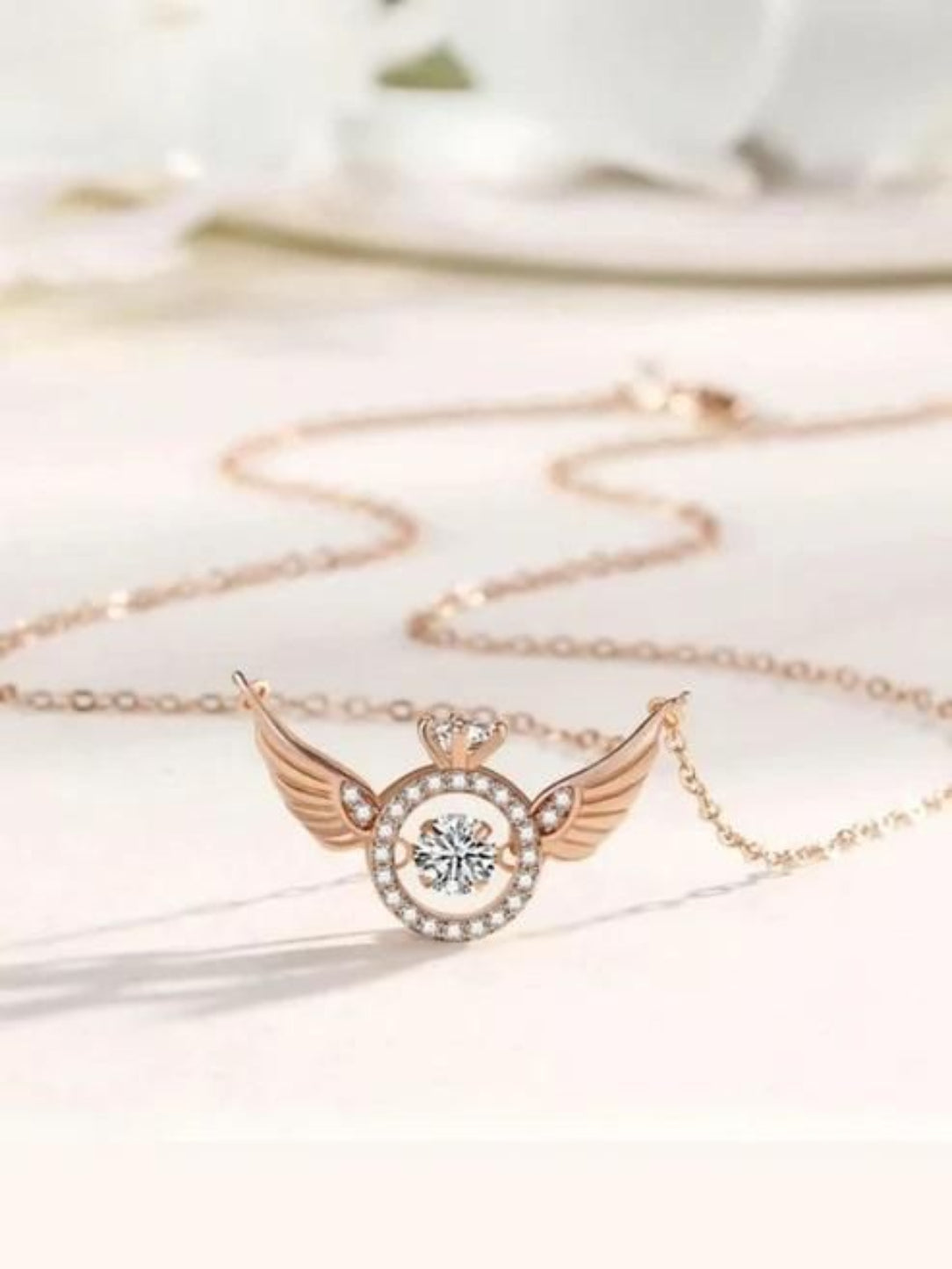 Rose gold necklace with a heart and wing design on a white background