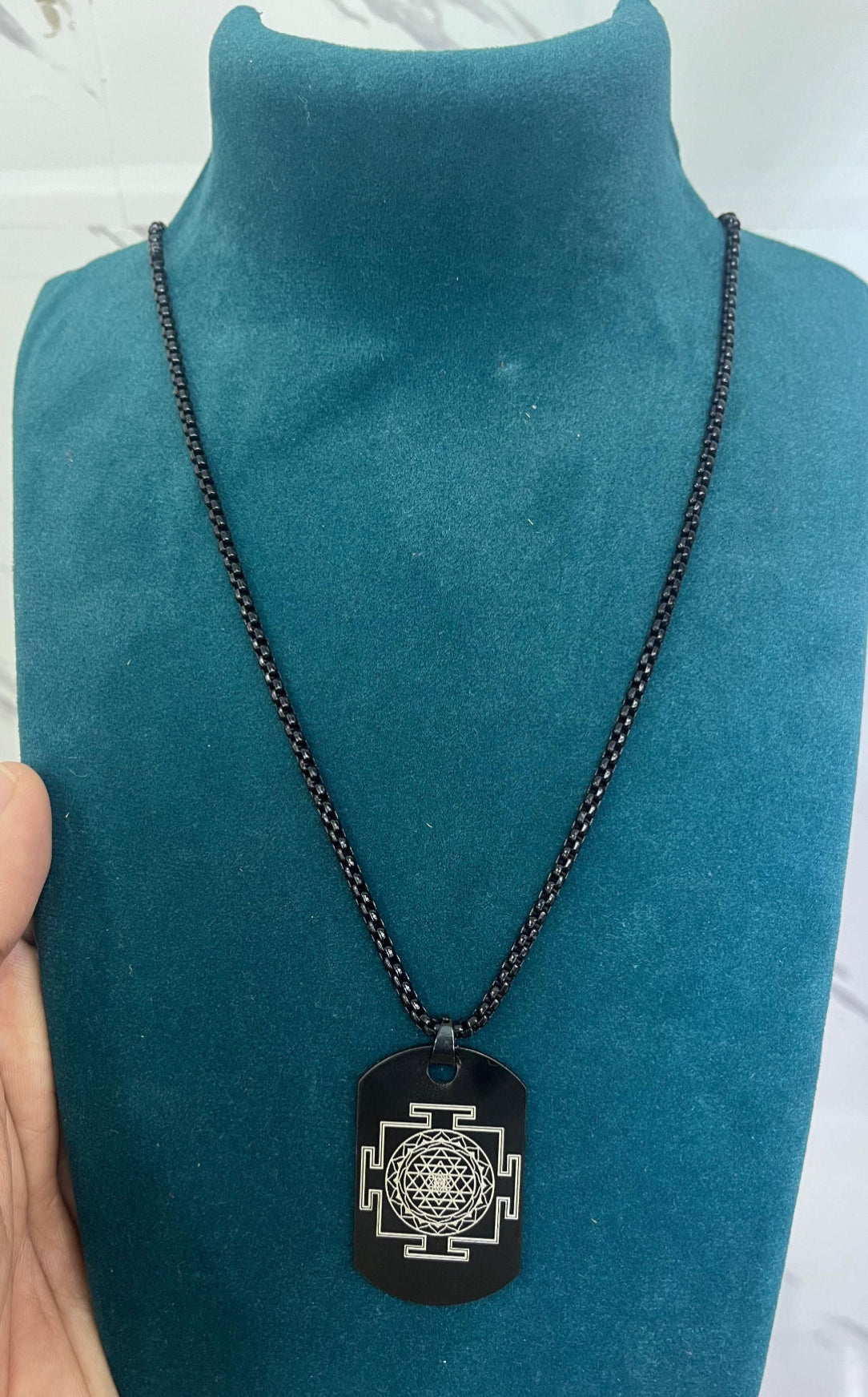 Black chain necklace with a pendant on a teal mannequin