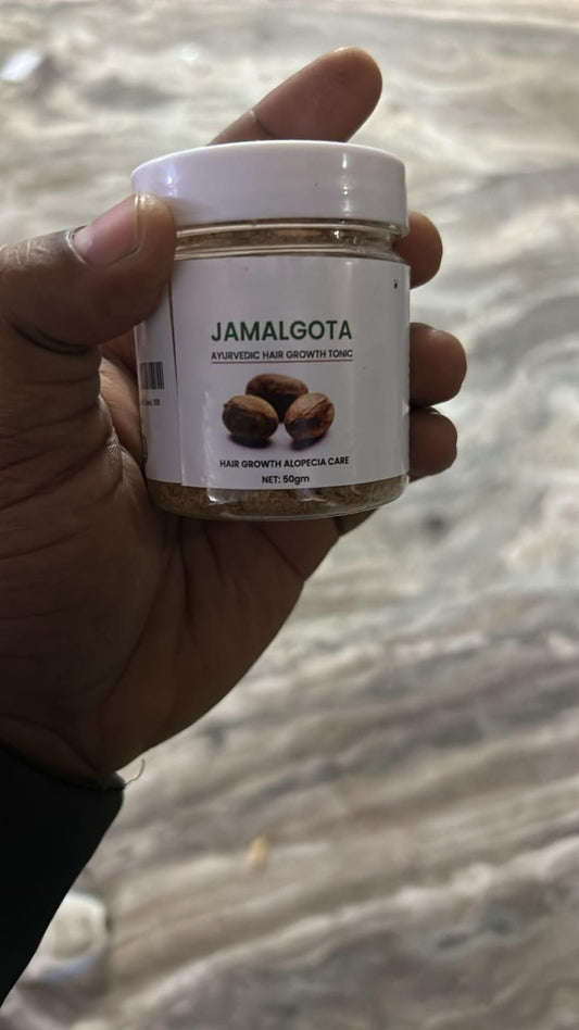 Hand holding a jar labeled 'Jamalgota' against a blurred background