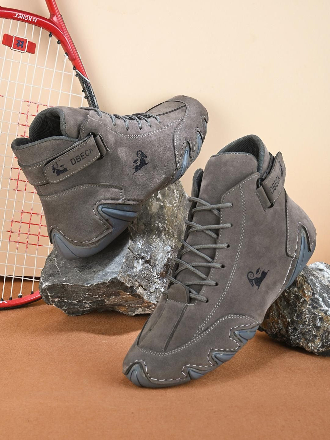 A pair of BOLLERO men's casual grey sneakers displayed on a rock with a badminton racket in the background.