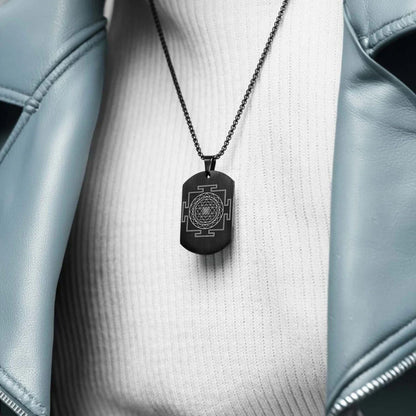 Black pendant necklace with a geometric design on a white shirt with a light blue jacket.