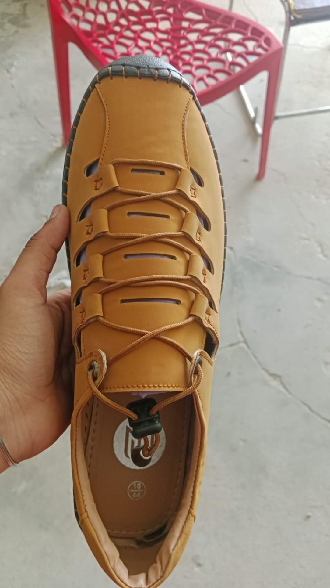 Yellow leather shoe held by a hand with a red chair in the background