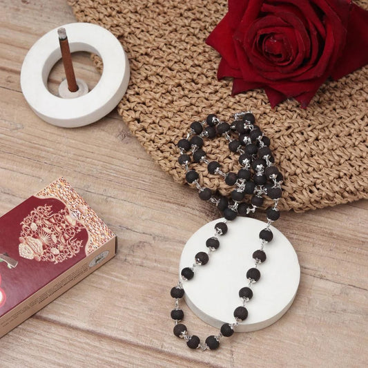 Black beaded necklace on a white base with a red rose and decorative box on a wooden surface