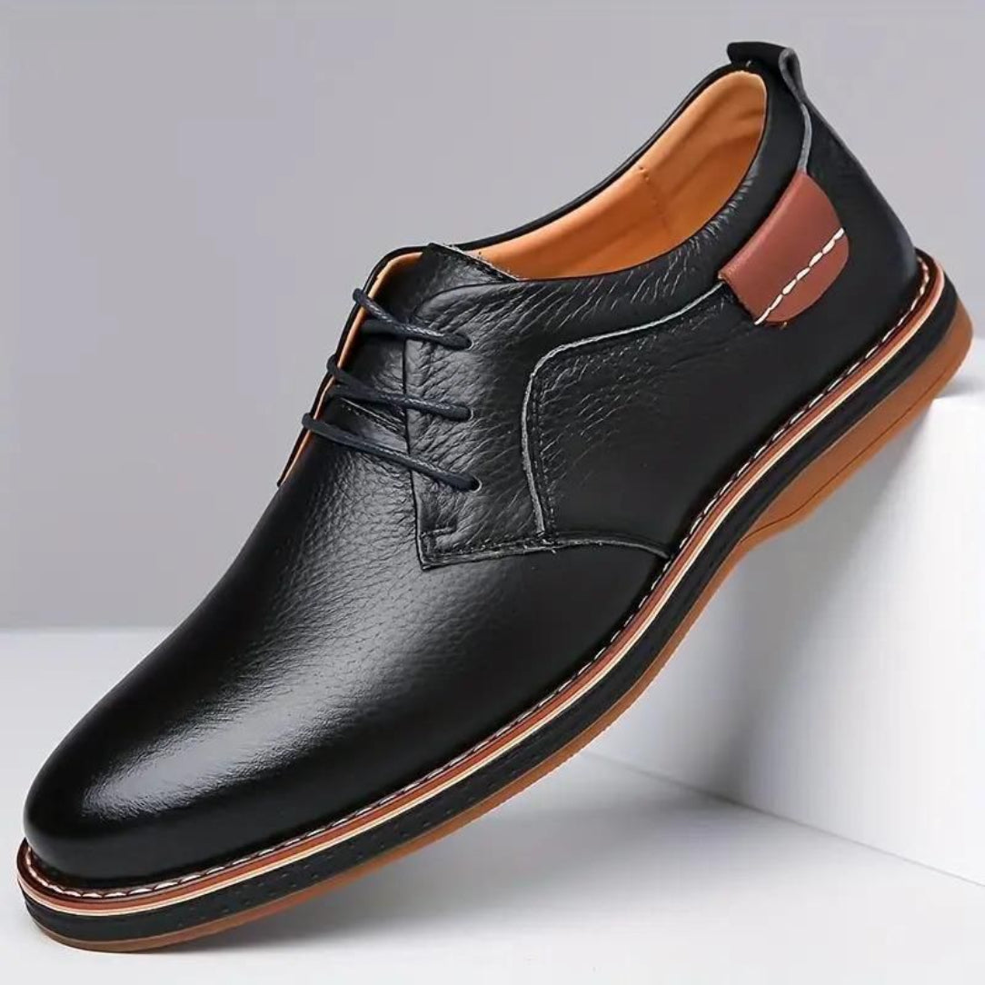 Black leather dress shoe with brown accents on a white background