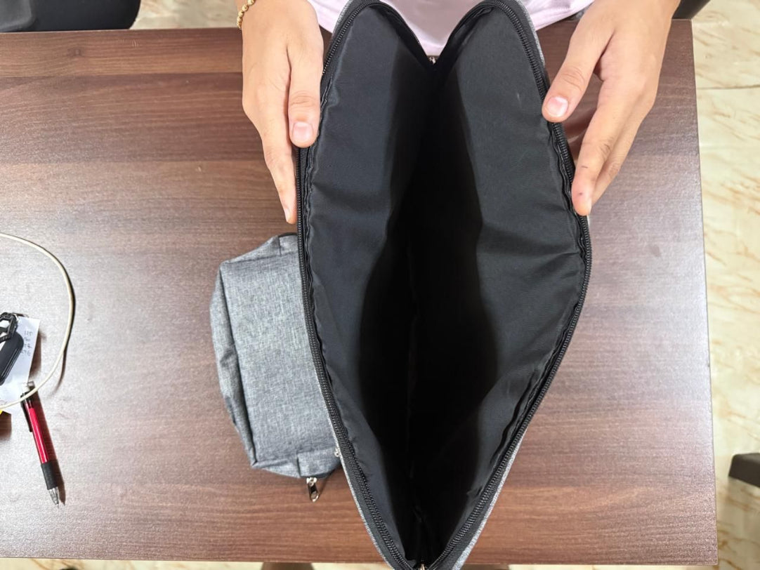Gray bag with a black interior held open by hands on a wooden surface.