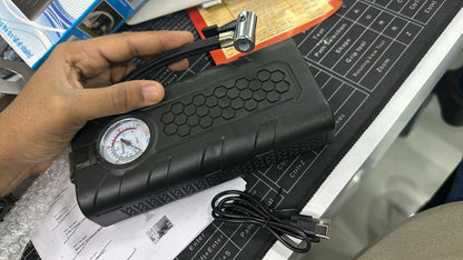 Hand holding a black portable air compressor on a workbench with tools and papers.