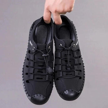 Black shoes with unique design held by a hand against a gray background