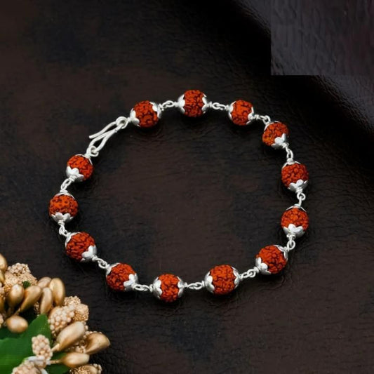 A silver-plated Rudraksha bracelet with red beads and silver accents, displayed against a dark background with floral embellishments.
