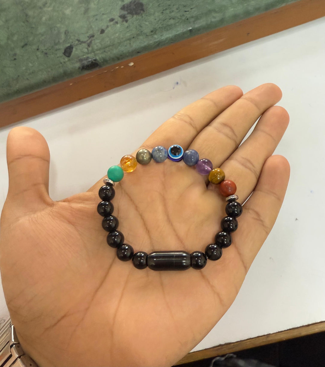Hand holding a colorful beaded bracelet on a white surface