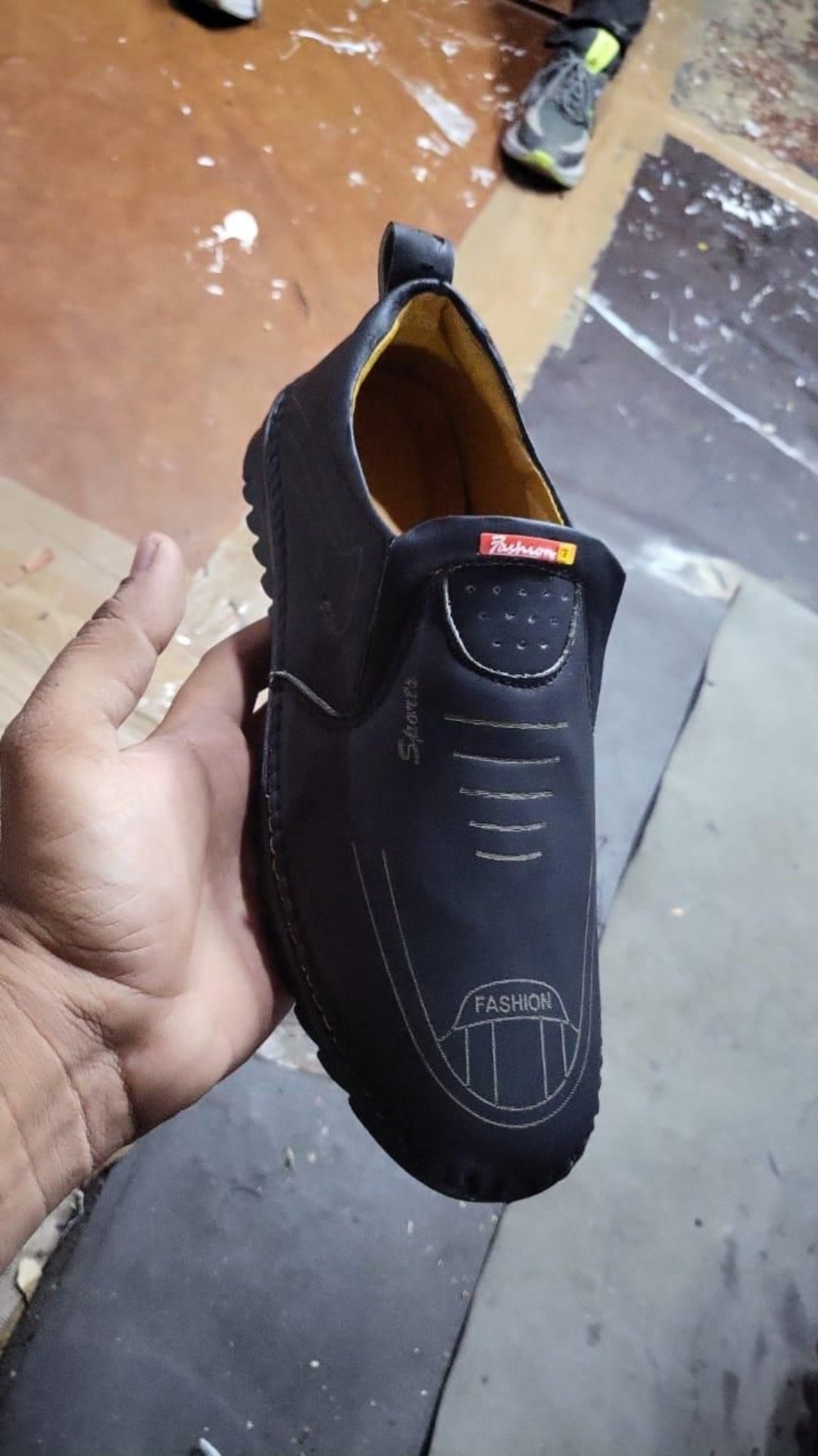 Black shoe held by a hand on a dark surface