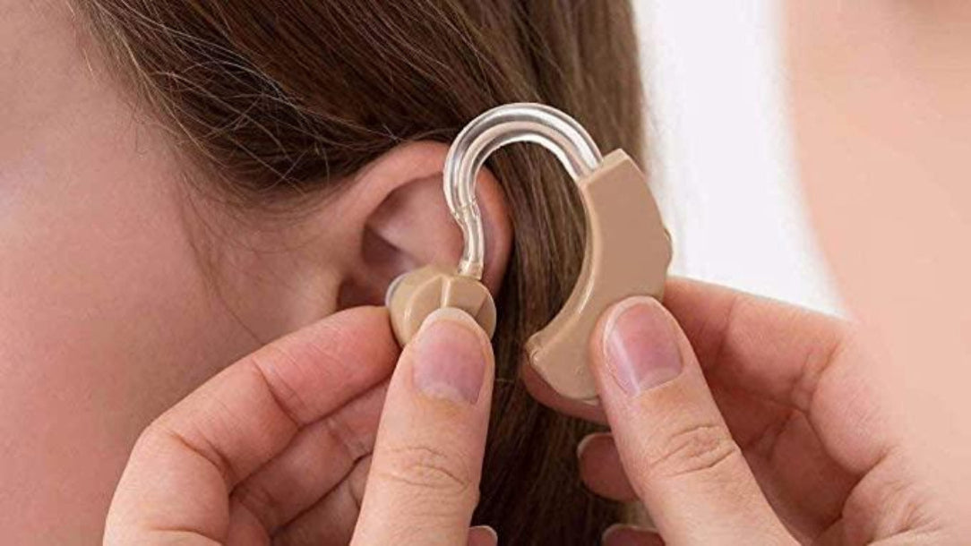 A person is fitting a beige hearing aid device into another person's ear.