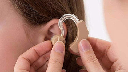 A person is fitting a beige hearing aid device into another person's ear.