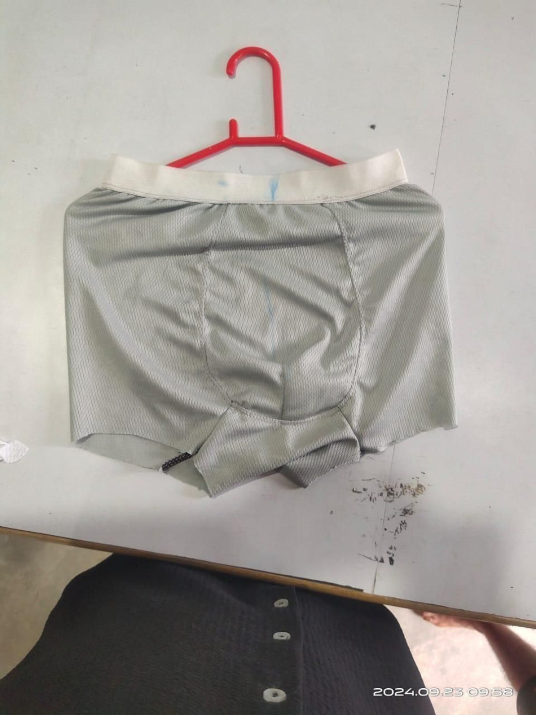 Gray boxer briefs on a red hanger against a white wall.