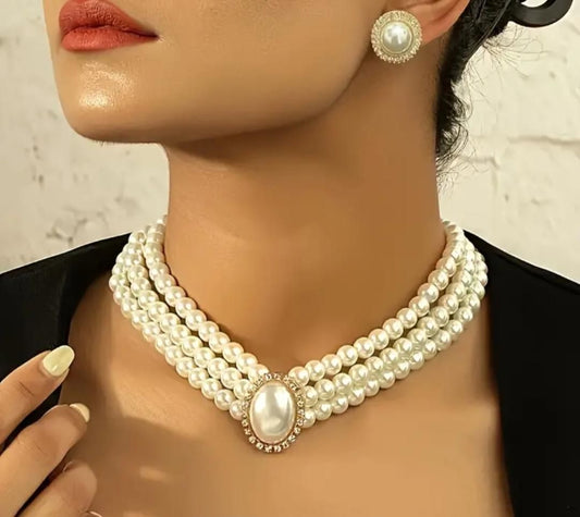A person showcasing an artificial pearl necklace with a prominent central pearl and smaller pearls strung around it, accompanied by matching earrings.