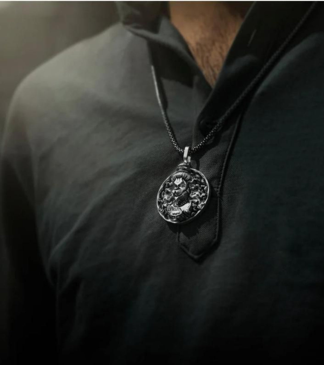Person wearing a dark shirt with a silver necklace featuring a detailed pendant.