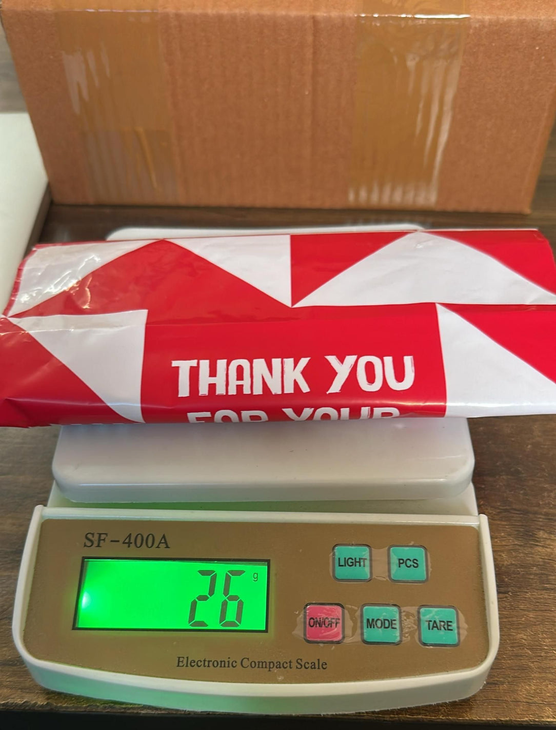 Digital scale displaying weight with a red and white box labeled 'Thank You' in the background.
