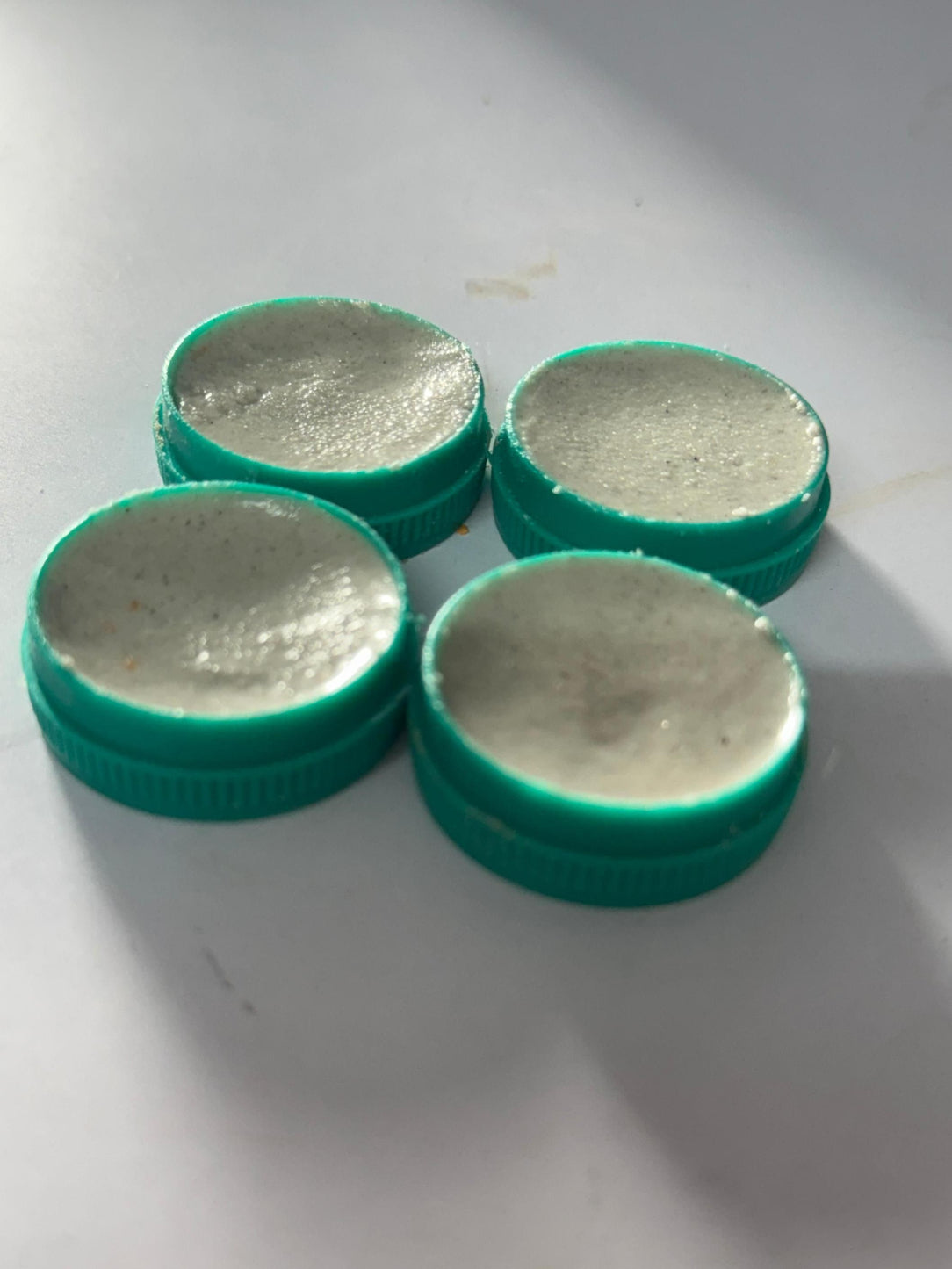 Four green bottle caps with metallic centers on a white surface