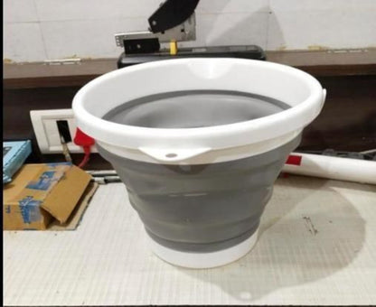 Collapsible gray bucket with white handle on a tiled floor.