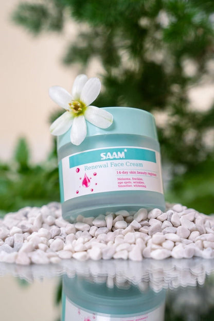 SAAM Renewal Face Cream jar with a white flower on a reflective surface and pebbles.