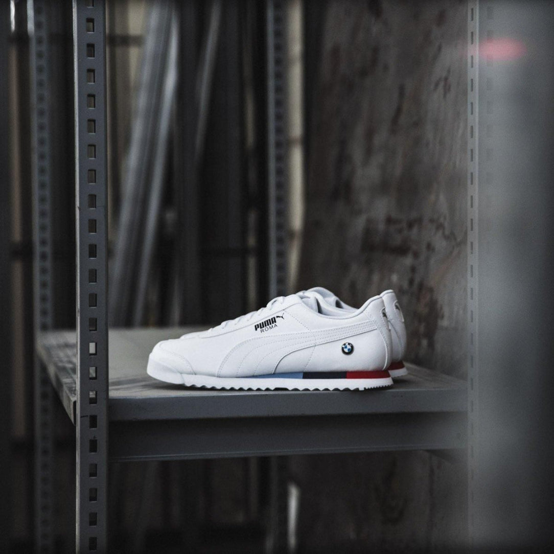 White sneaker with BMW logo on a metal shelf against a dark background