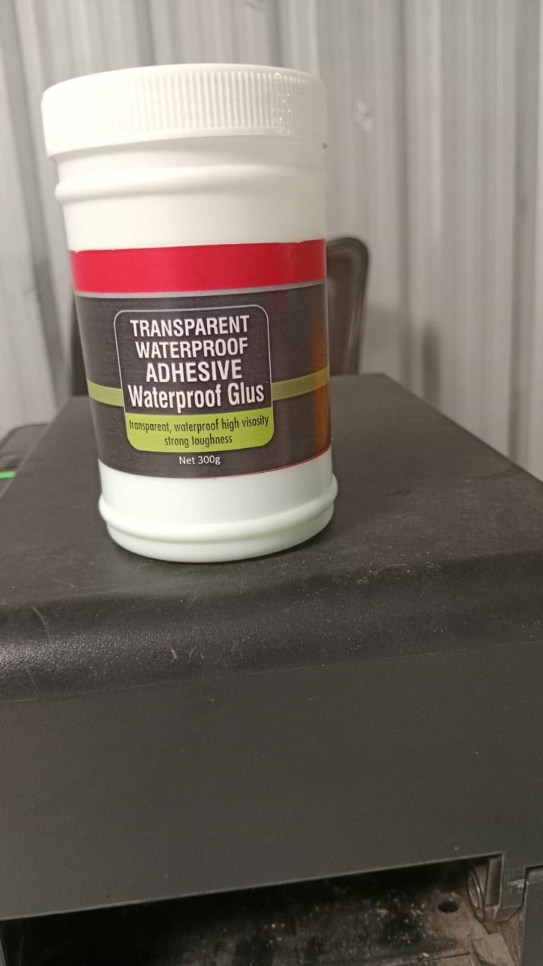 Jar of transparent waterproof adhesive on a dark surface