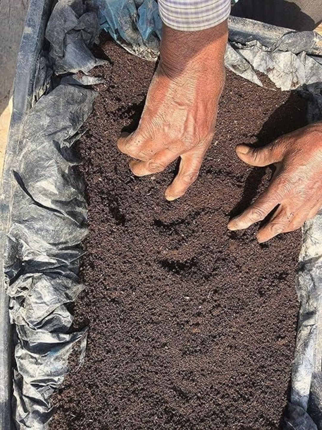 Person handling a piece of dark brown soil or compost on a black plastic sheet.